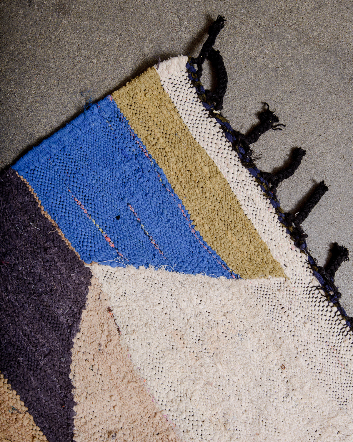 Corner of vintage kelim rug with black cotton tassels.